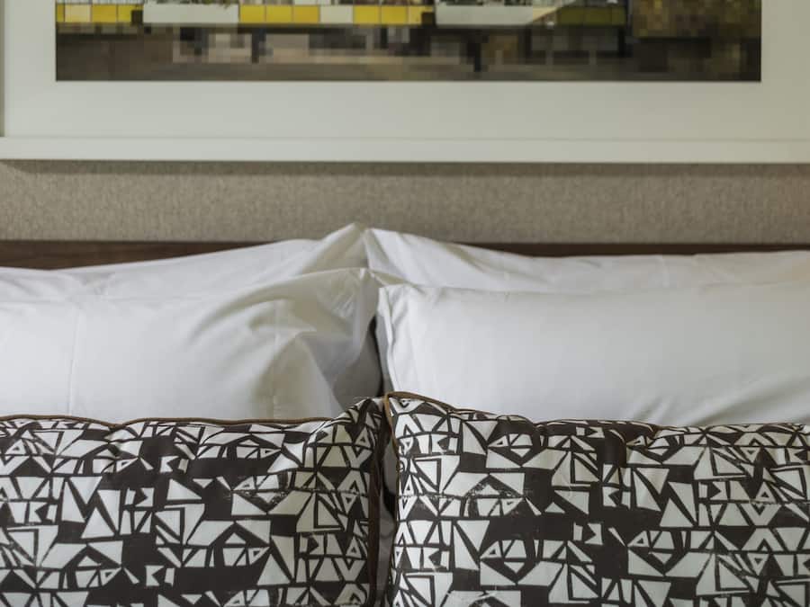 A hotel room with a bed, pillows, and a framed cityscape picture on the wall.