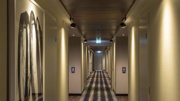 A hotel hallway with a patterned carpet, wall-mounted lights, and doors with signage.