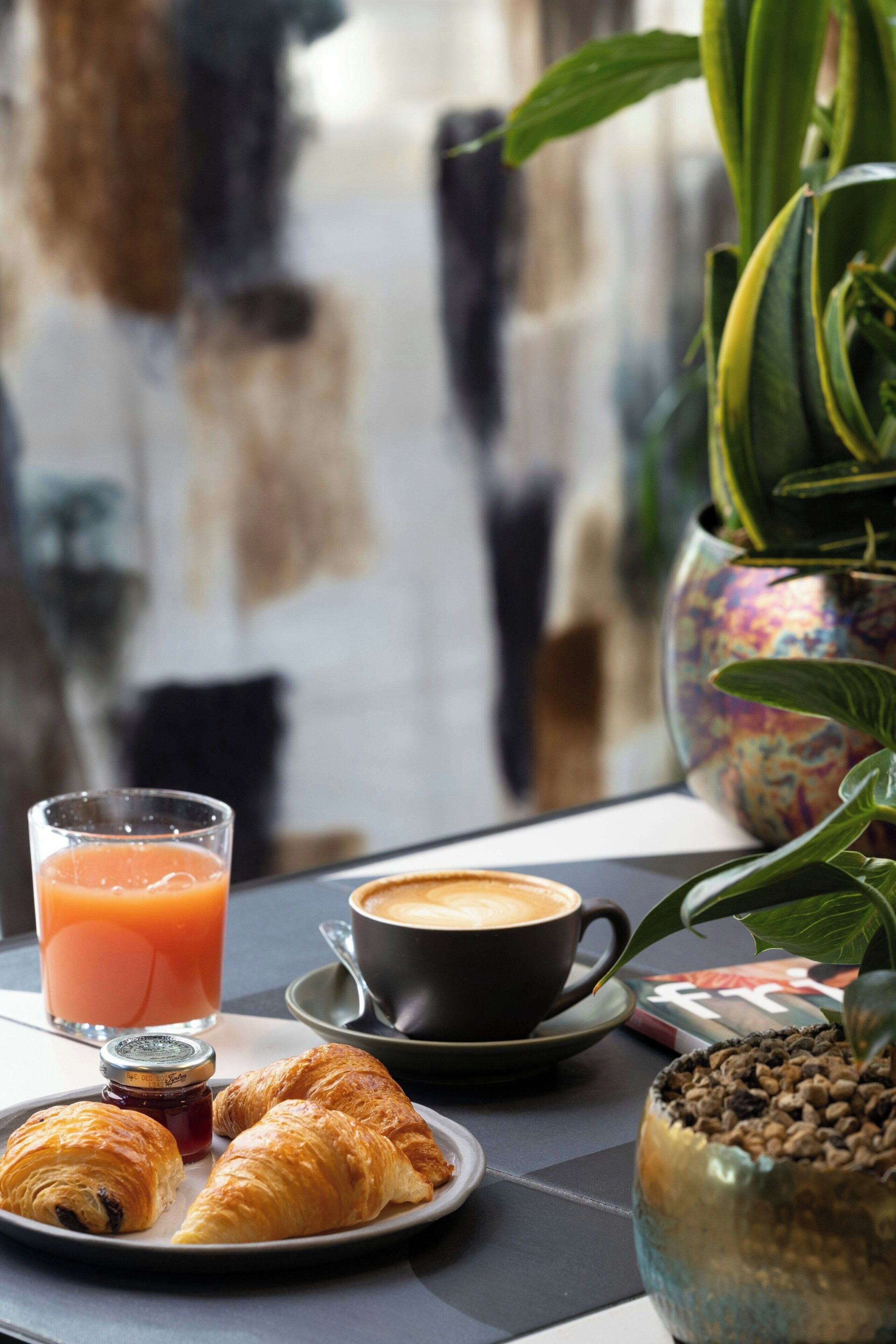 Colazione con croissant, un bicchiere di succo d'arancia, una tazza di caffè e una pianta in vaso.