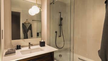 A modern bathroom with a glass-enclosed shower, a white sink, and a mirror with a towel hanging on the wall.