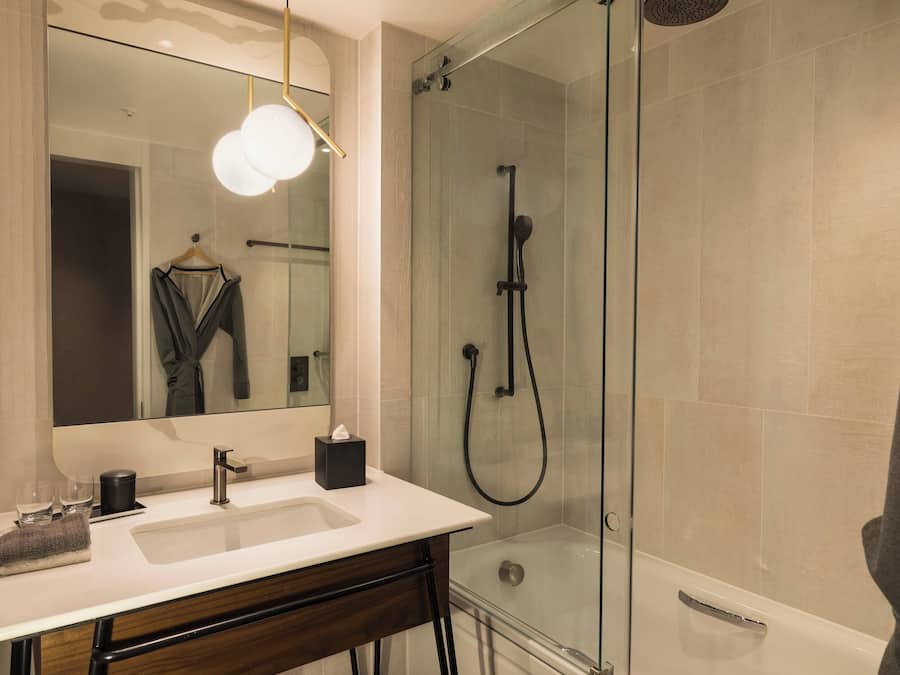 A modern bathroom with a glass-enclosed shower, a white sink, and a mirror with a towel hanging on the wall.