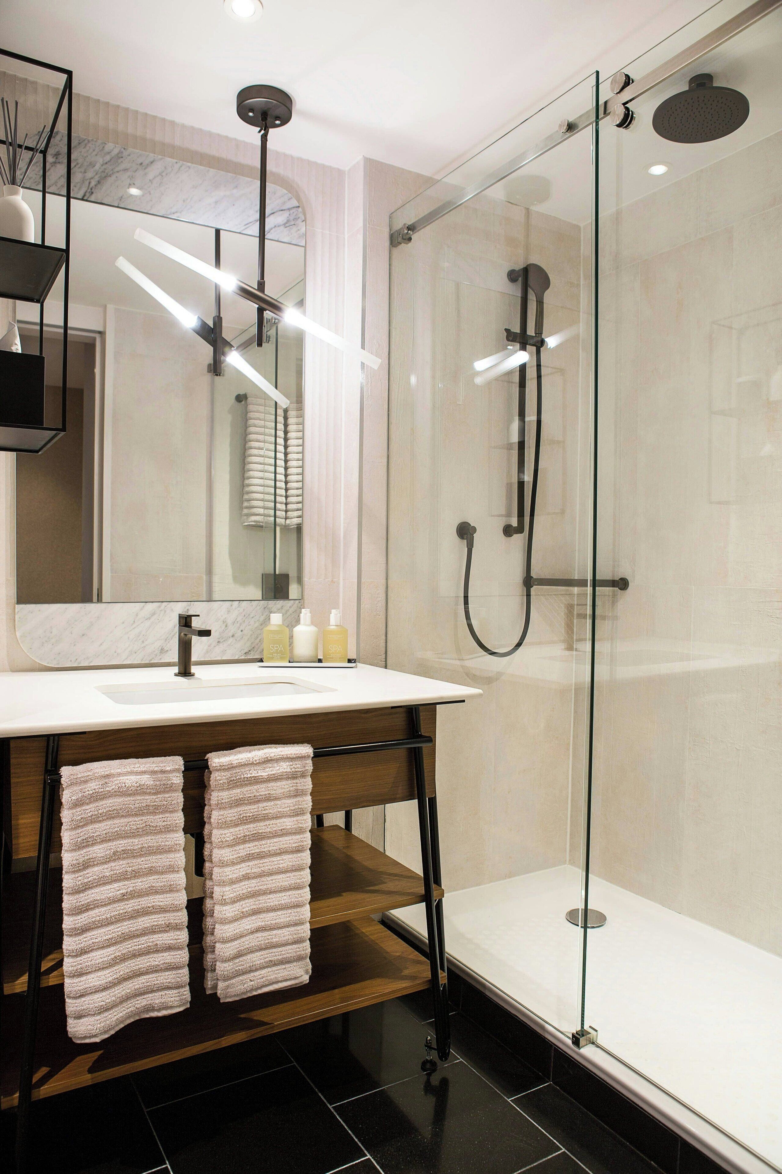 Een moderne badkamer met een douchecabine van glas, een marmeren wastafelmeubel en netjes opgevouwen handdoeken.