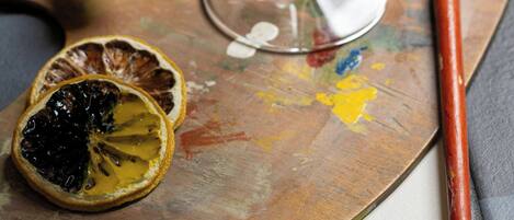 A cocktail glass with a dried orange slice garnish on a palette with paint and a brush.