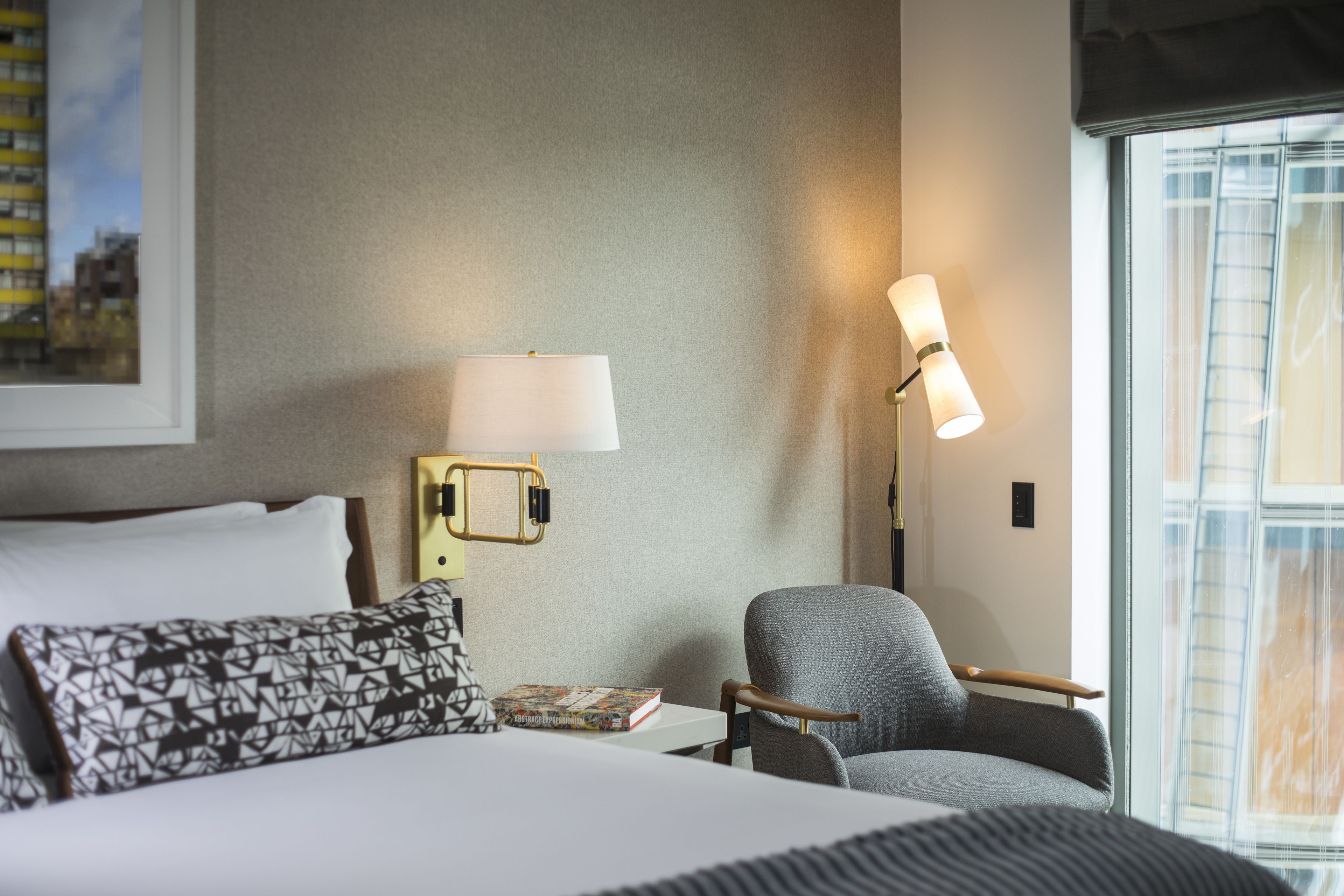 A hotel room with a bed, a chair, a lamp, and a framed picture on the wall.