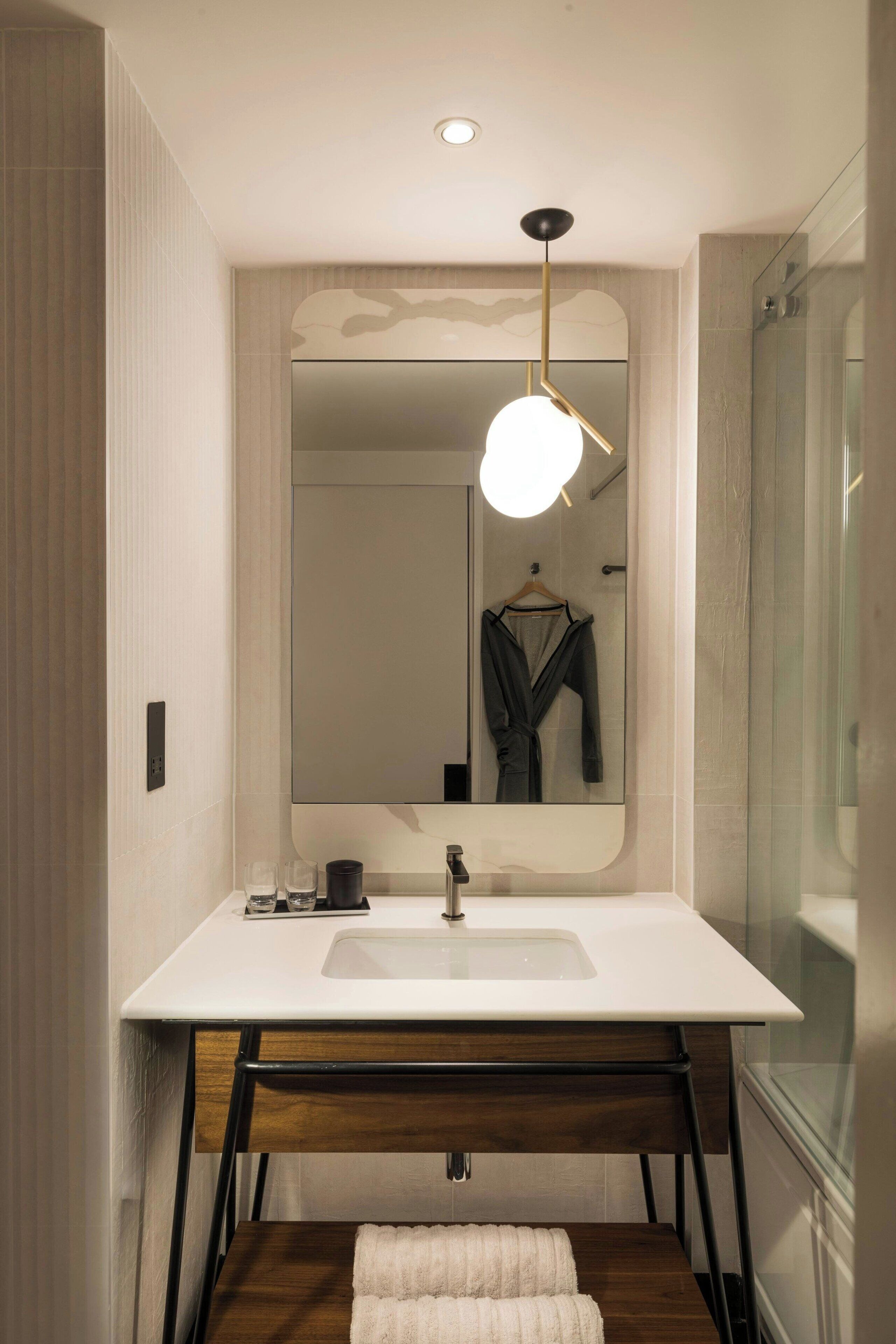 Un bagno moderno con uno specchio grande, un lavandino bianco e un mobile contenitore in legno.