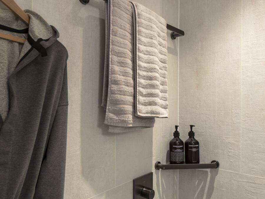 Une salle de bain avec un porte-serviettes sur lequel est pliée une serviette, une étagère avec deux bouteilles et une serviette accrochée au mur.