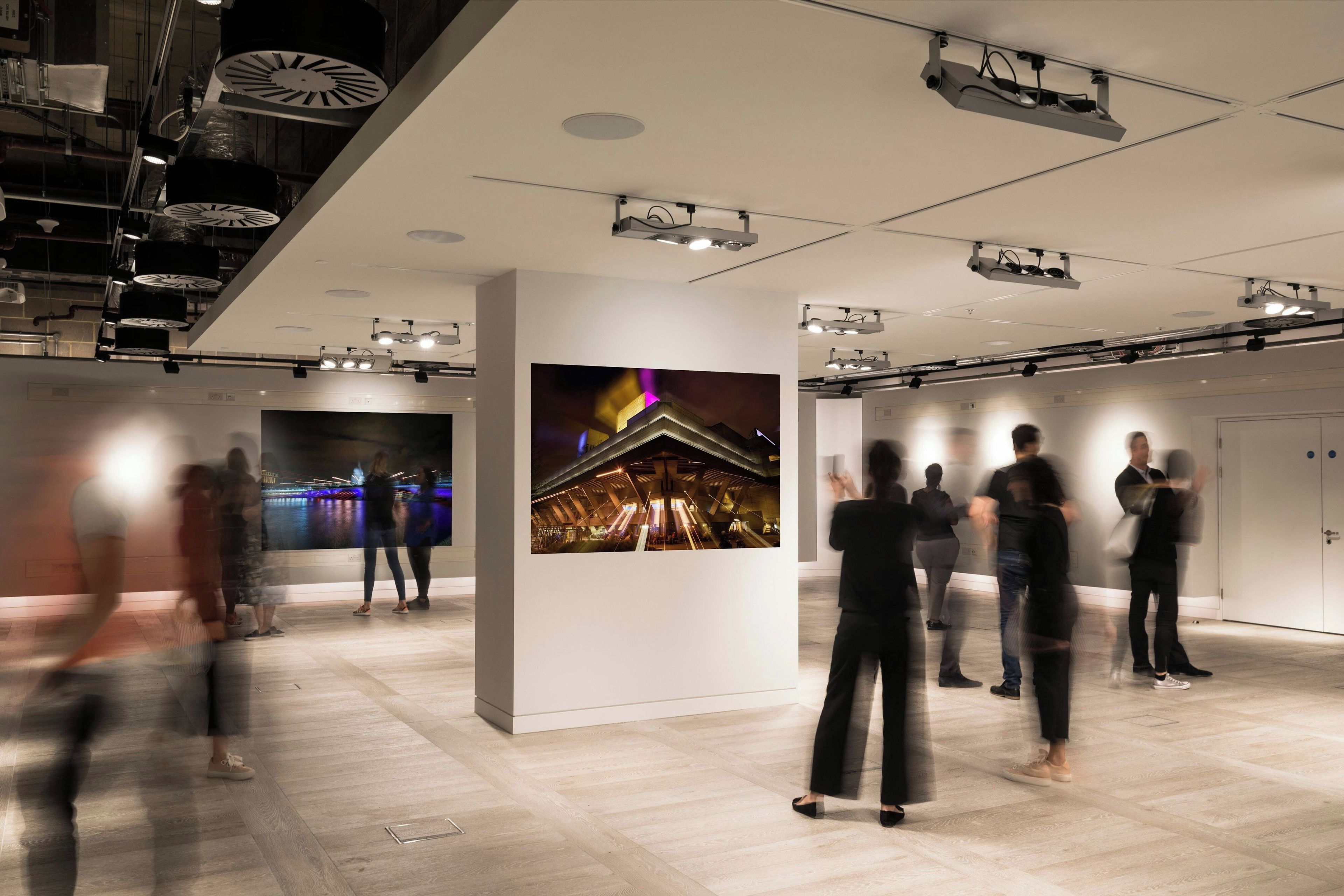 An indoor art gallery with a modern design, featuring a large central artwork and multiple ceiling-mounted lights.