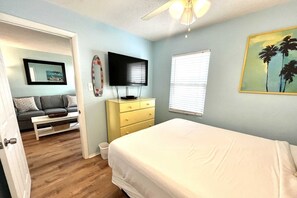 A bedroom with a bed, a television, a dresser, a window with blinds, and a painting on the wall. - Sunrise Ge 104 2 Bedroom Condo by RedAwning (Gulf Shores)