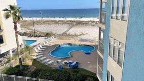 A pool area with lounge chairs and a small pool, overlooking a beach and the ocean.