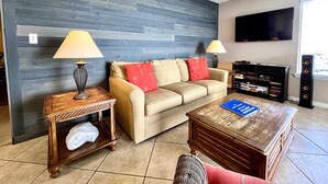 A living room with a sofa, two side tables with lamps, a coffee table, a bookshelf, and a television mounted on the wall.