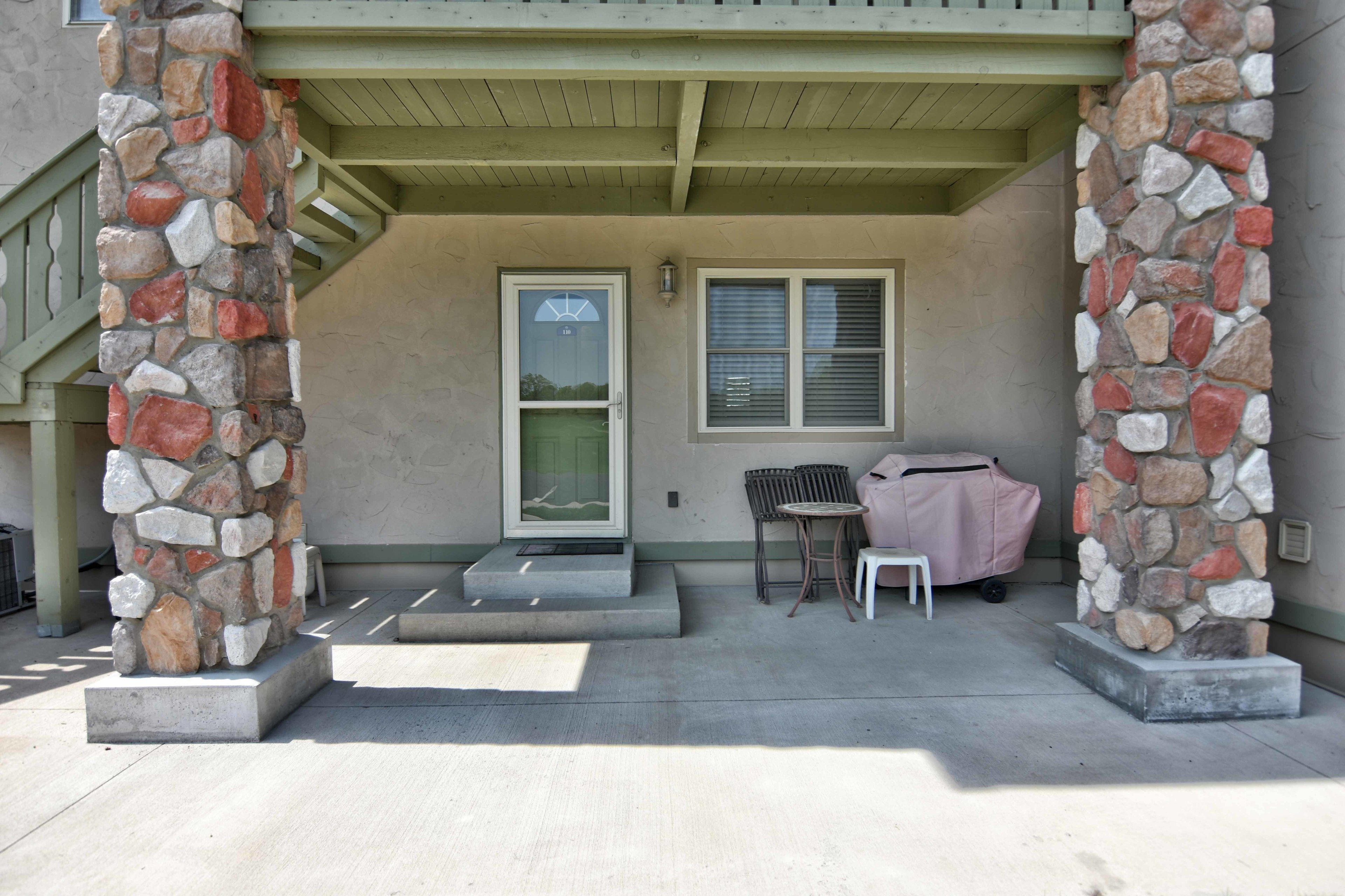 A covered porch with stone pillars, a door, and a window with blinds.