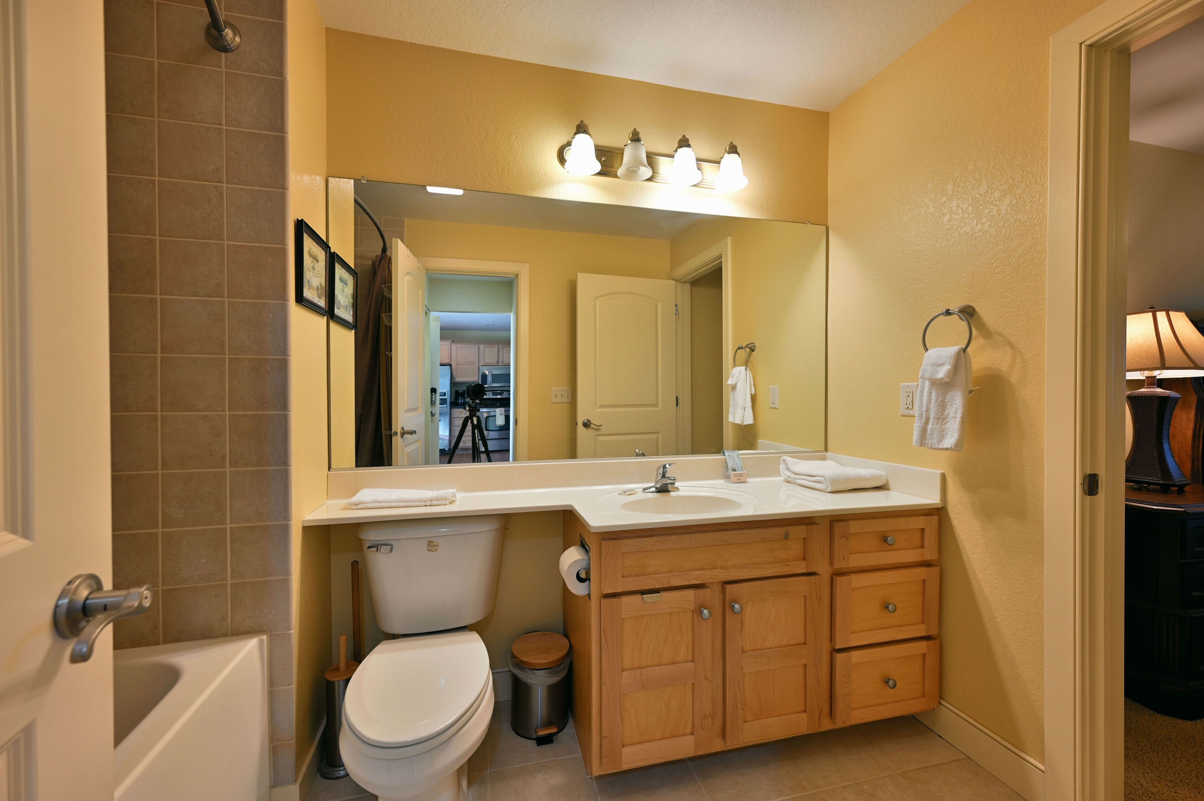 A modern bathroom with a white toilet, wooden vanity, and a large mirror.