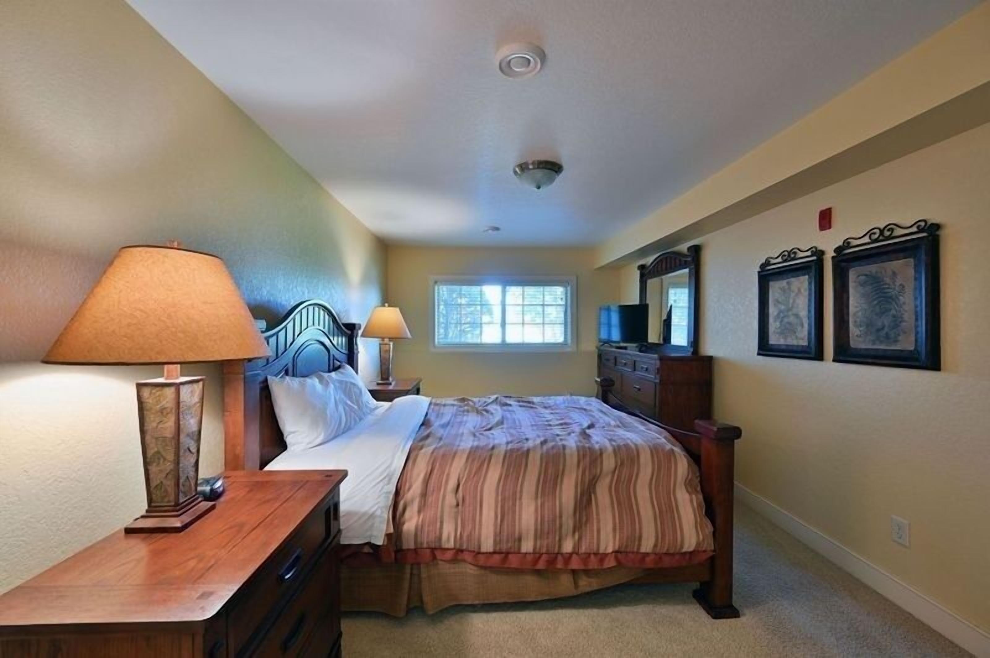A bedroom with a bed, two bedside tables, a lamp, a dresser, and framed artwork on the wall.
