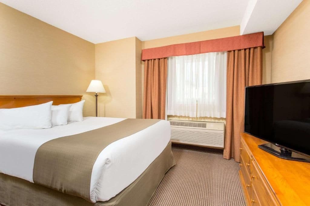 Una camera d'albergo con un letto, una televisione, una lampada e una finestra con tende.