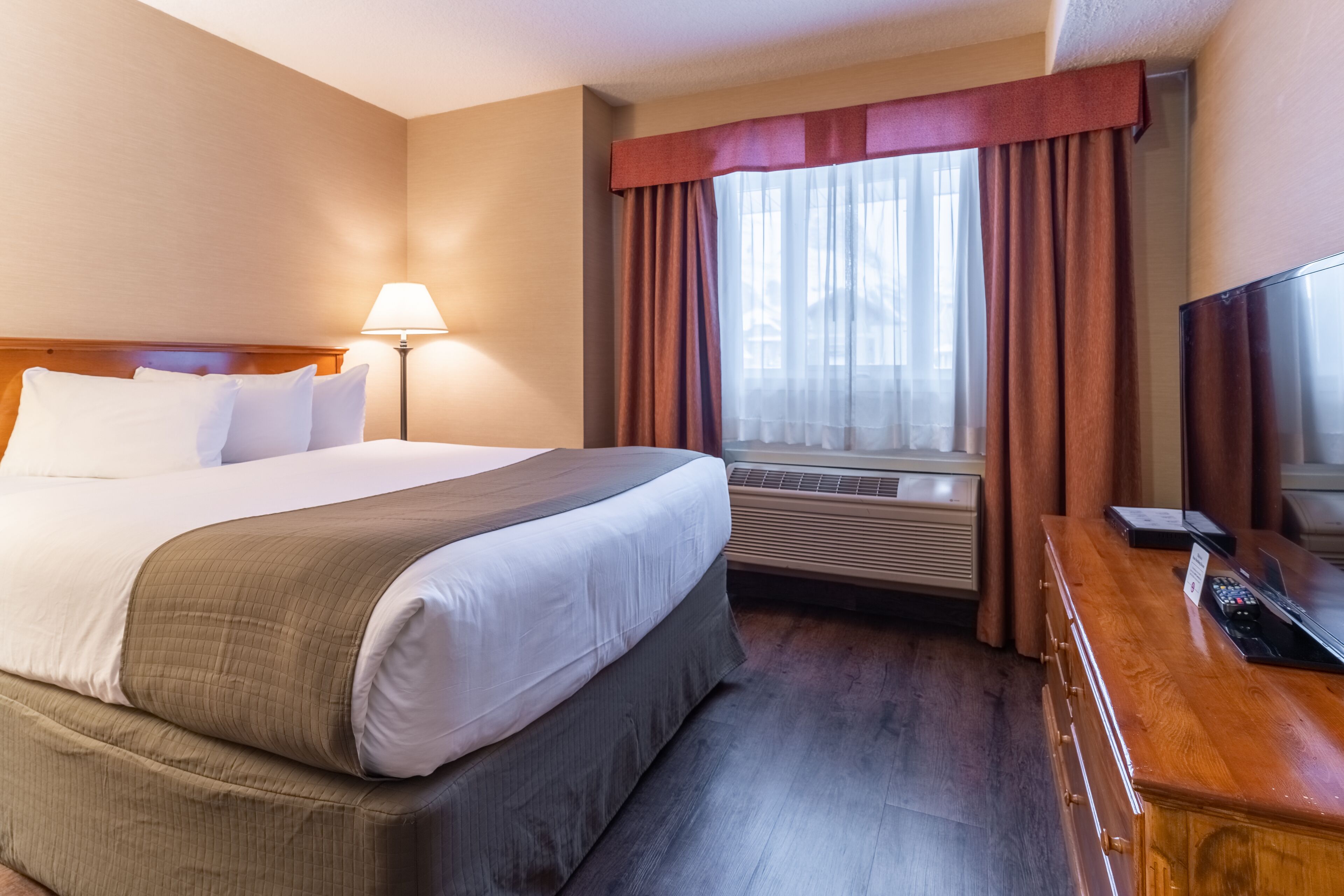 A hotel room with a large bed, a desk, and a window with curtains.
