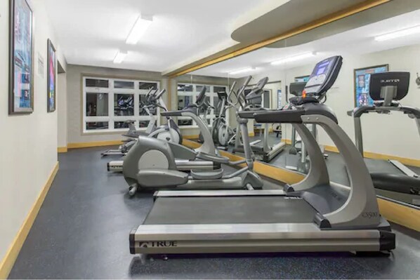 Ein Fitnessraum mit Laufbändern, Crosstrainern und einer Spiegelwand.