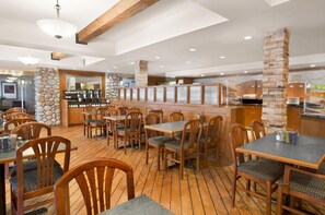 A restaurant with wooden tables and chairs, stone walls, and a bar area.