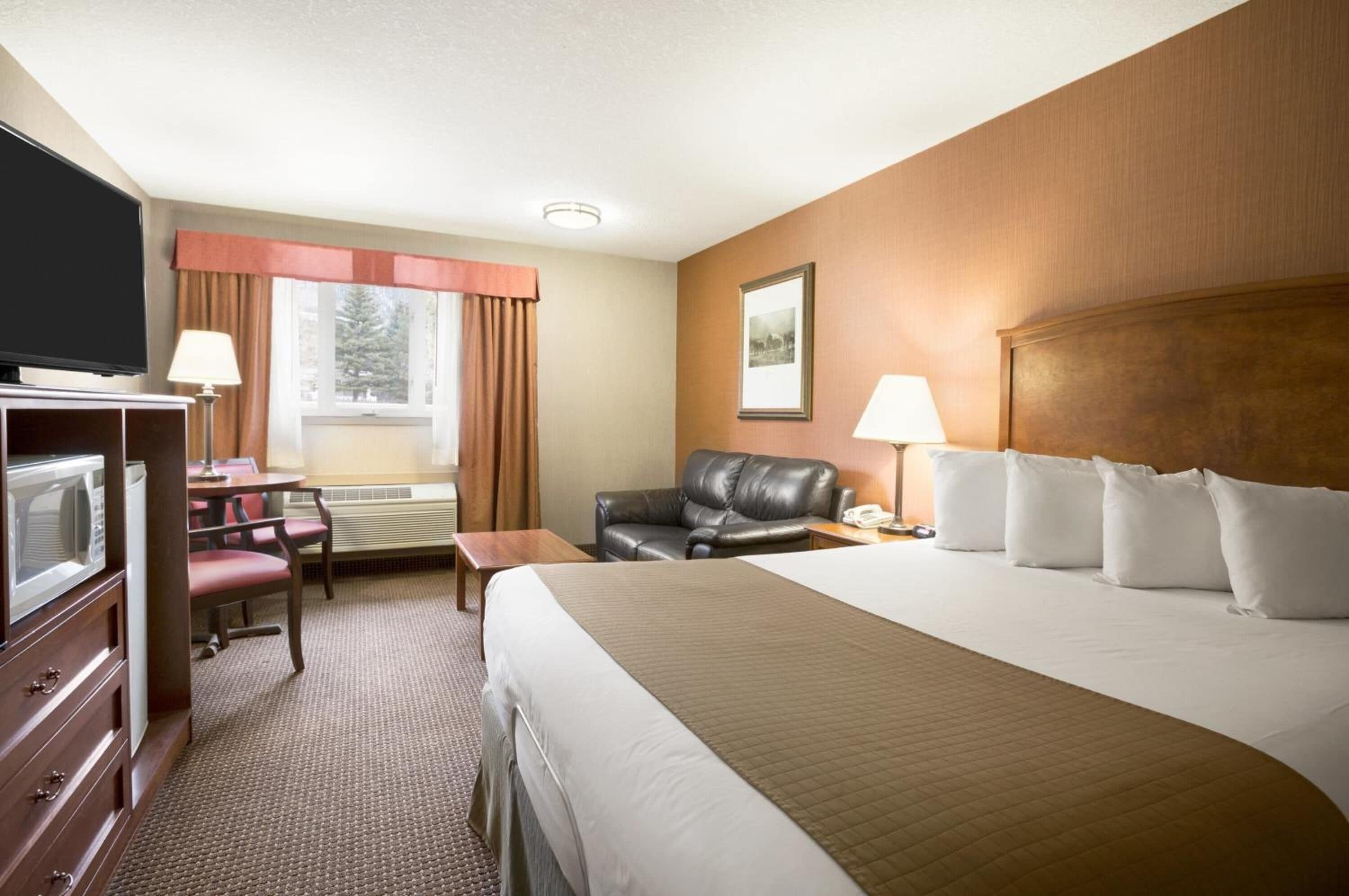 A hotel room with a bed, a TV, a desk with a lamp, a chair, and a window with curtains.