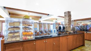 A breakfast bar with a variety of pastries and fruits, wooden cabinets, and a stone pillar. - Canmore Inn & Suites (Canmore)