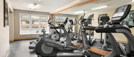 Un gimnasio con bicicletas estáticas, cintas de correr y un espejo grande.