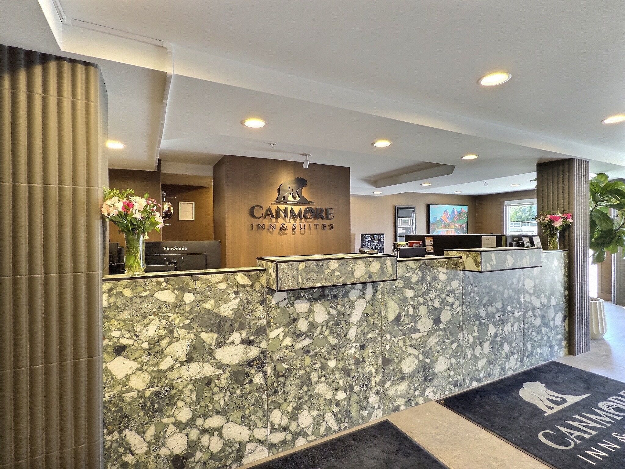 Un área de recepción con mostrador de mármol, el logo de Canmore Inn & Suites y un mostrador de recepción.
