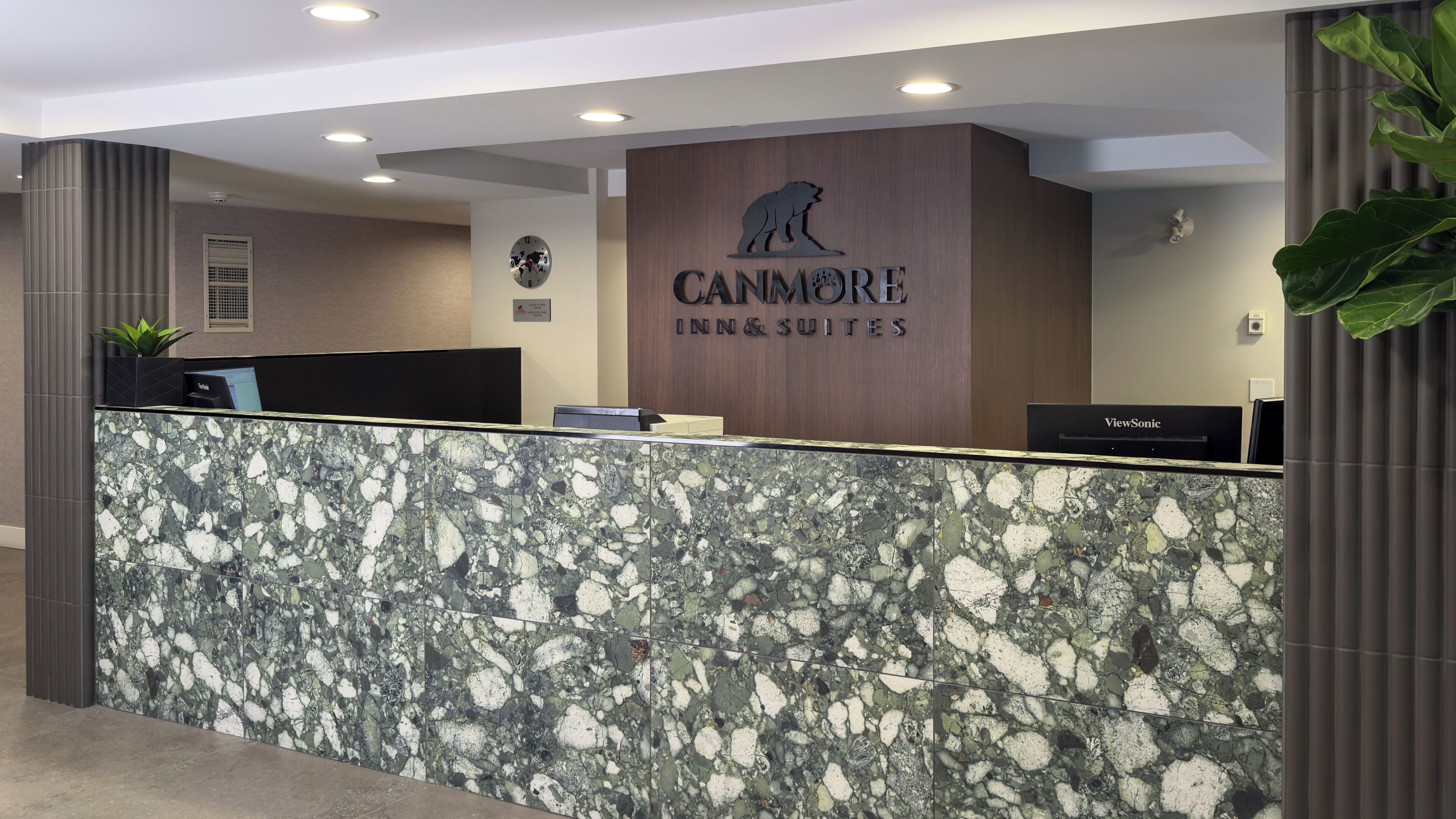 A reception desk with a marble top, a clock, and a sign for Canmore Inn & Suites.
