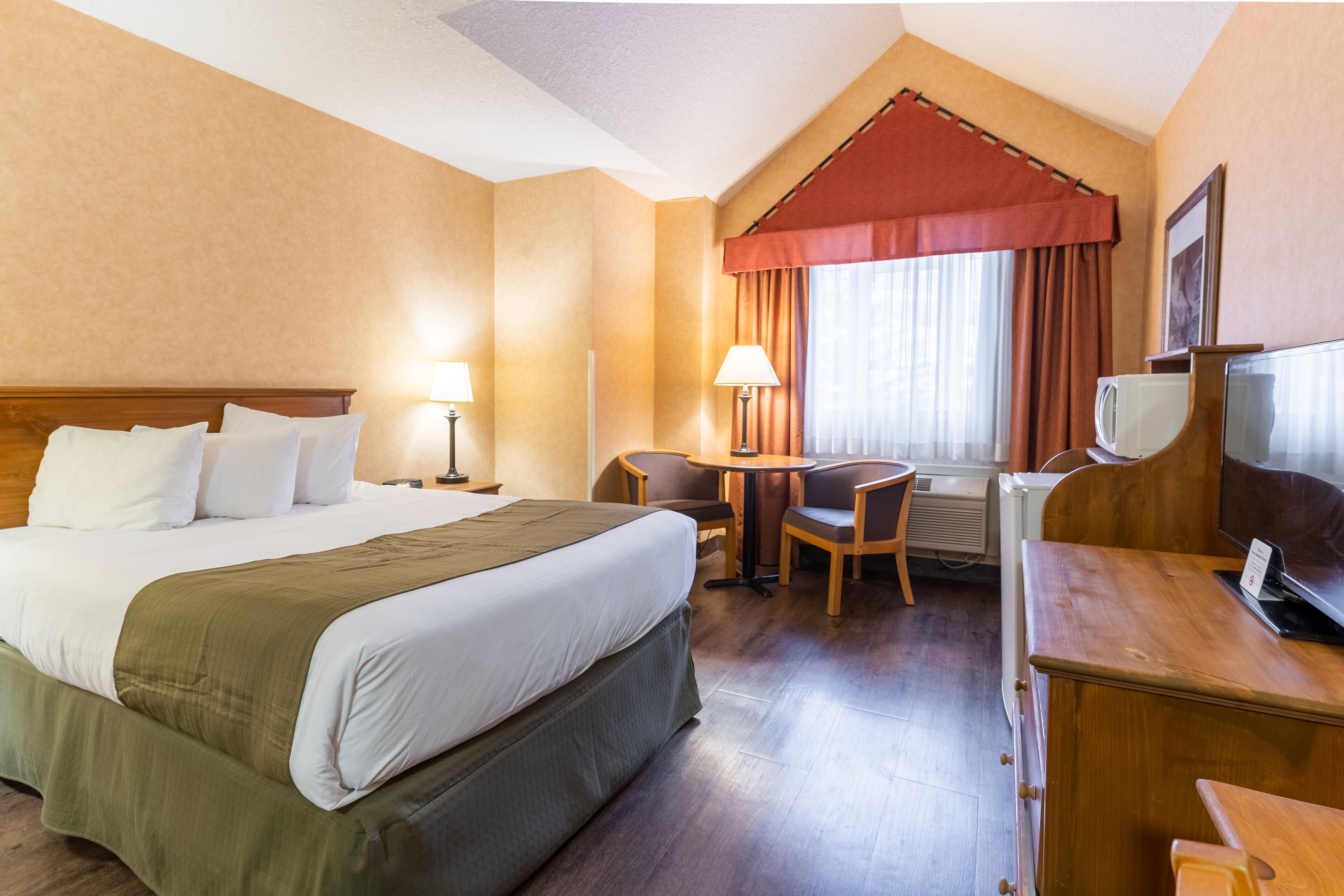 A hotel room with a large bed, a desk with a chair, a small table, and a television.