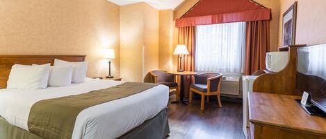 A hotel room with a large bed, a desk with a chair, a small table, and a television.