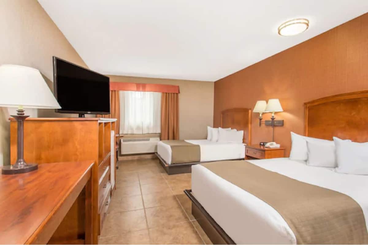 A hotel room with a TV, two beds, a desk, and a lamp.