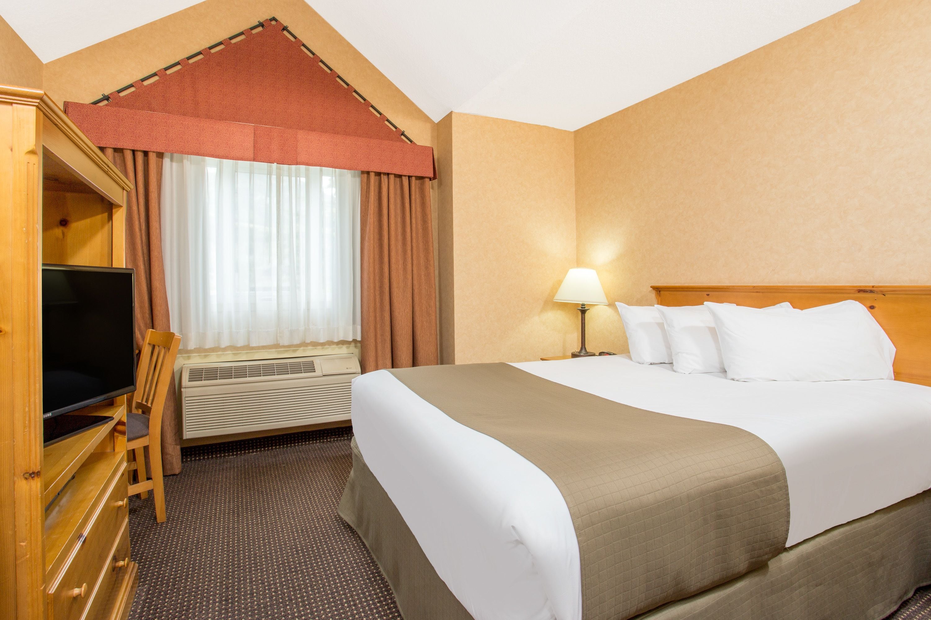 A hotel room with a large bed, a television, a desk, and a window with curtains.
