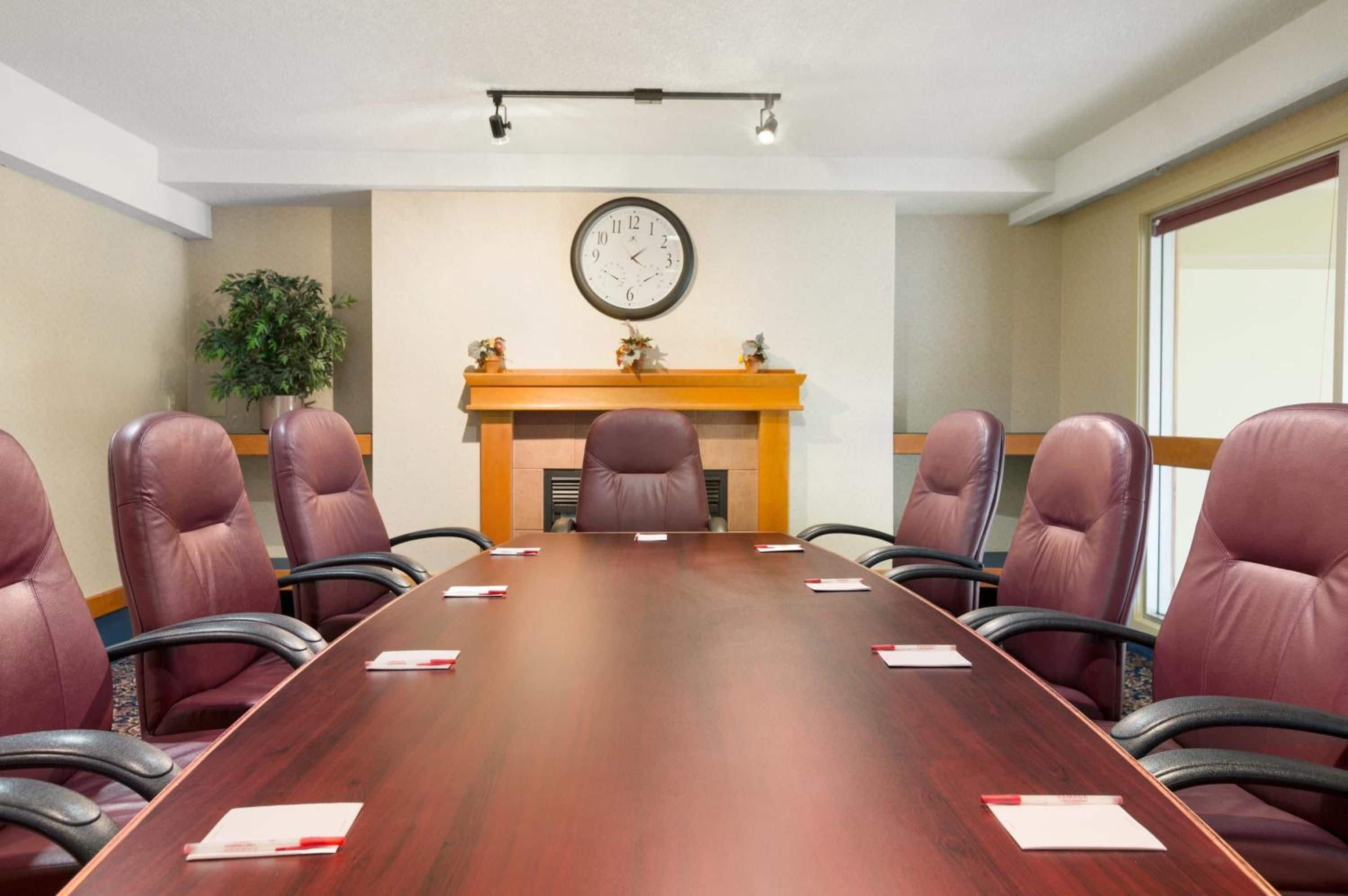 Un salón de conferencias con una mesa larga, seis sillas, un reloj, una chimenea y una planta.