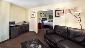 A hotel room with a kitchenette, a bed, a leather sofa, and a coffee table.
