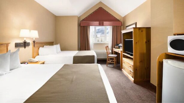 A hotel room with two beds, a desk, a chair, a TV, and a refrigerator. - Canmore Inn & Suites (Canmore)