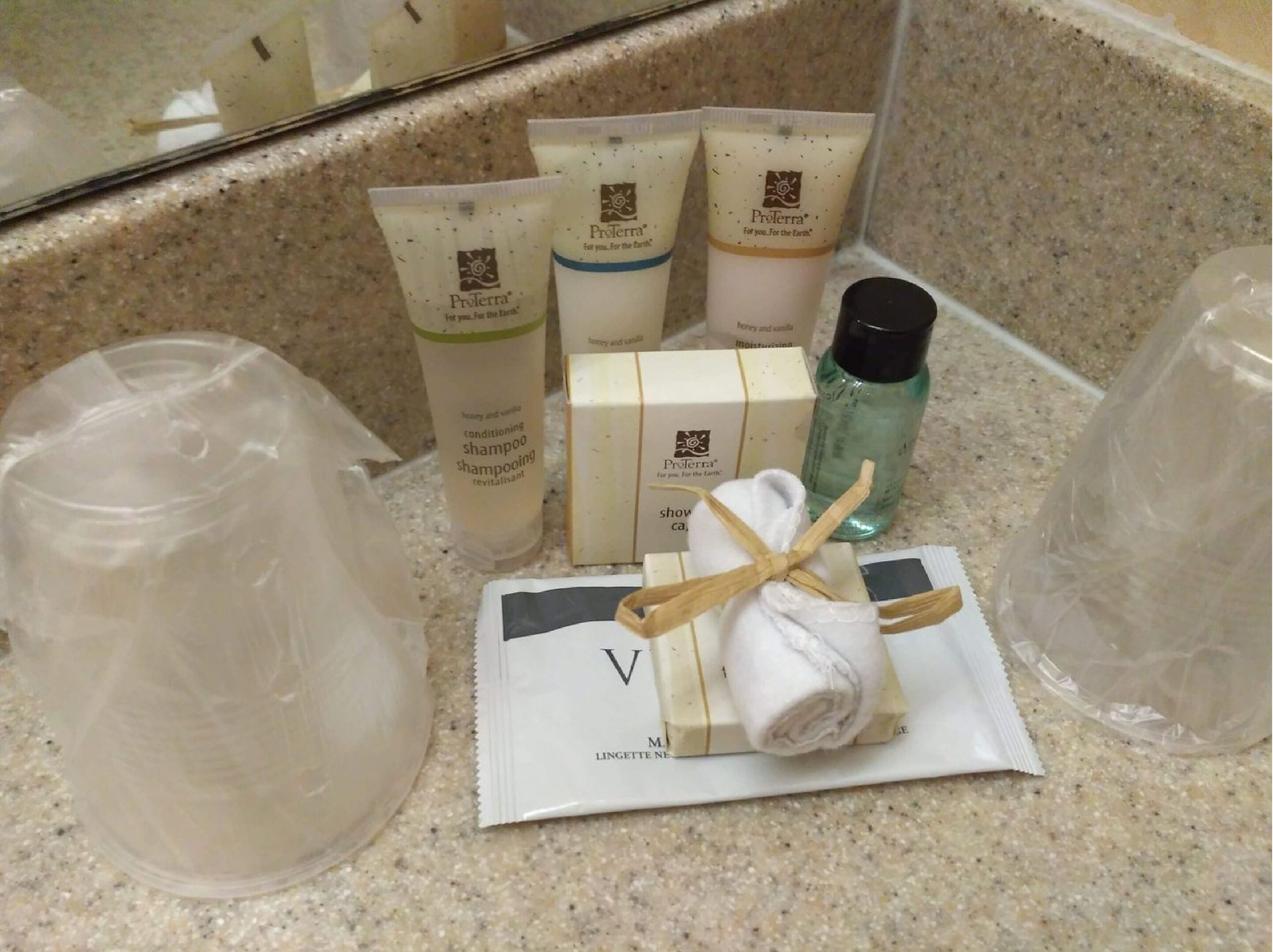 Toiletartikler, herunder Proterra shampoo, et håndklæde og en flaske flydende sæbe på en badeværelsesbordplade.