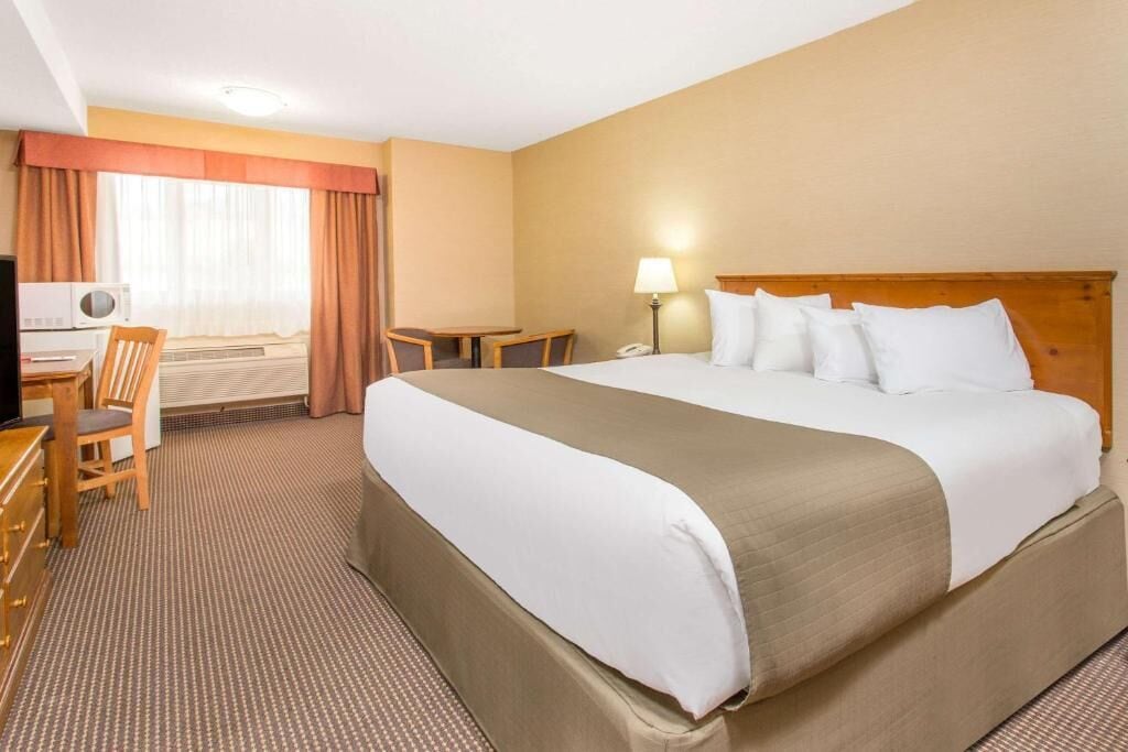A hotel room with a large bed, a desk with a chair, a television, and a lamp.