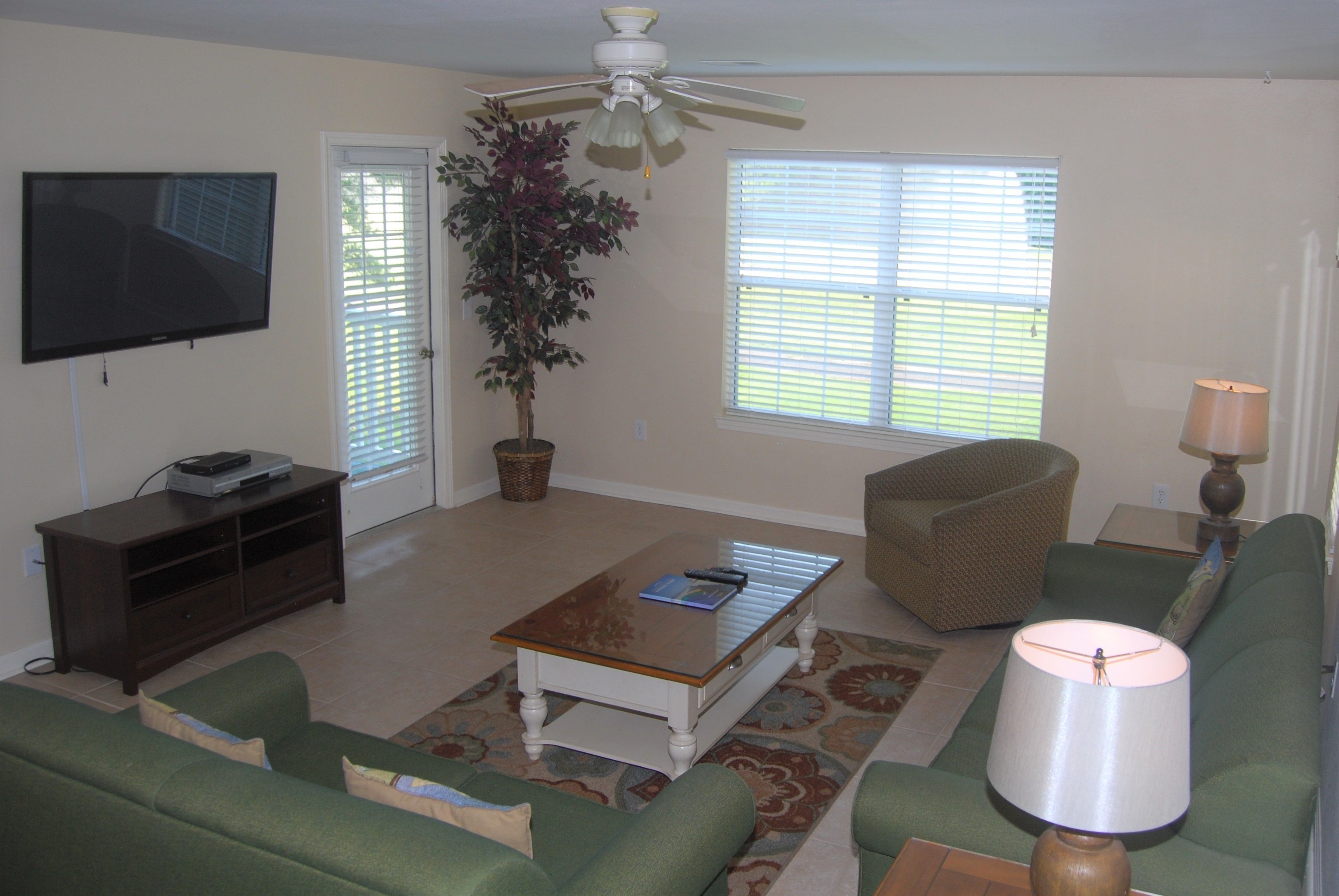A living room with a television, a ceiling fan, a potted plant, a coffee table, a sofa, a chair, and a lamp.