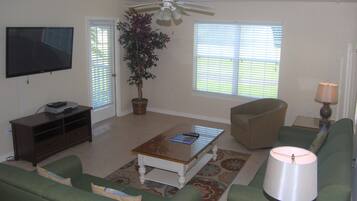 A living room with a television, a ceiling fan, a potted plant, a coffee table, a sofa, a chair, and a lamp.