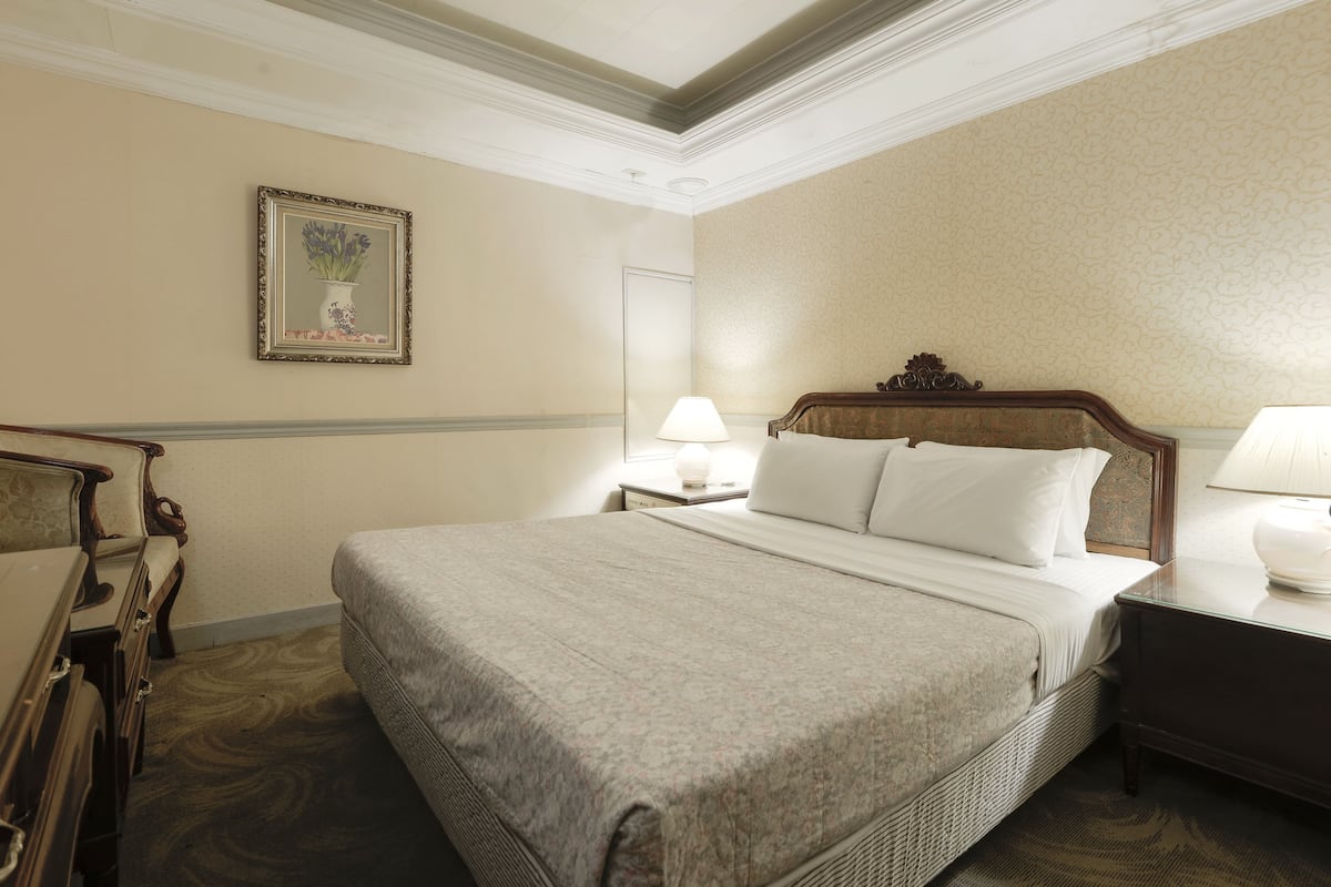 A neatly arranged hotel room with a large bed, a nightstand, a lamp, and a dresser.