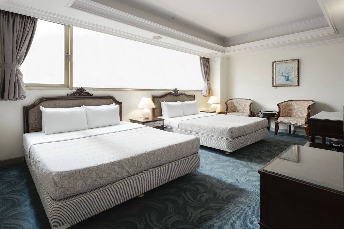 A hotel room with two beds, a desk, a chair, and a television.
