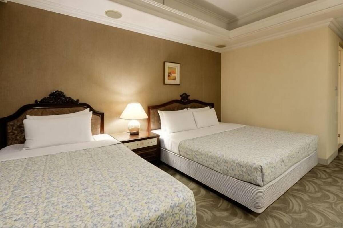 A hotel room with two beds, a nightstand with a lamp, and a framed picture on the wall.