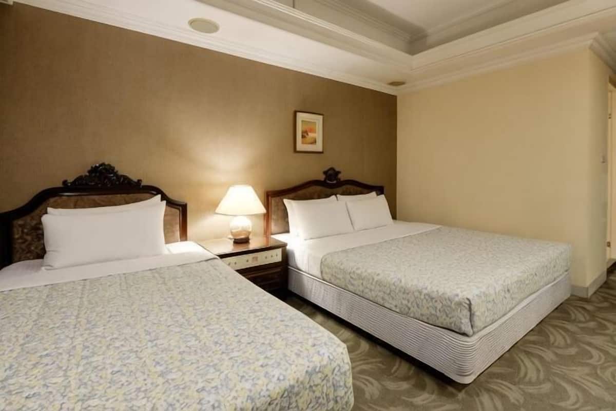 Una habitación de hotel con dos camas, una mesita de noche con lámpara y un cuadro en la pared.