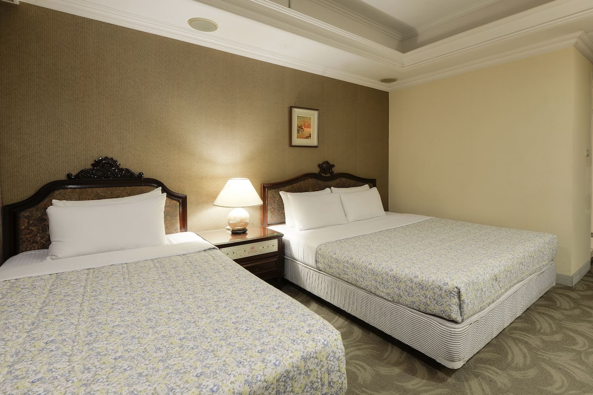 A hotel room with two beds, a nightstand with a lamp, and a framed picture on the wall.