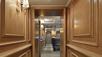 A hallway with wooden paneling and patterned carpet, leading to a room with a black metal railing.