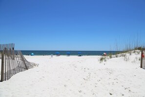 A sandy beach with a wooden fence, several beach umbrellas, and a clear blue sky.