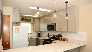 A modern kitchen with white cabinets, a stainless steel microwave, a stove, and pendant lights. - Ocean Reef 702 3 Bedroom Townhouse by RedAwning (Gulf Shores)