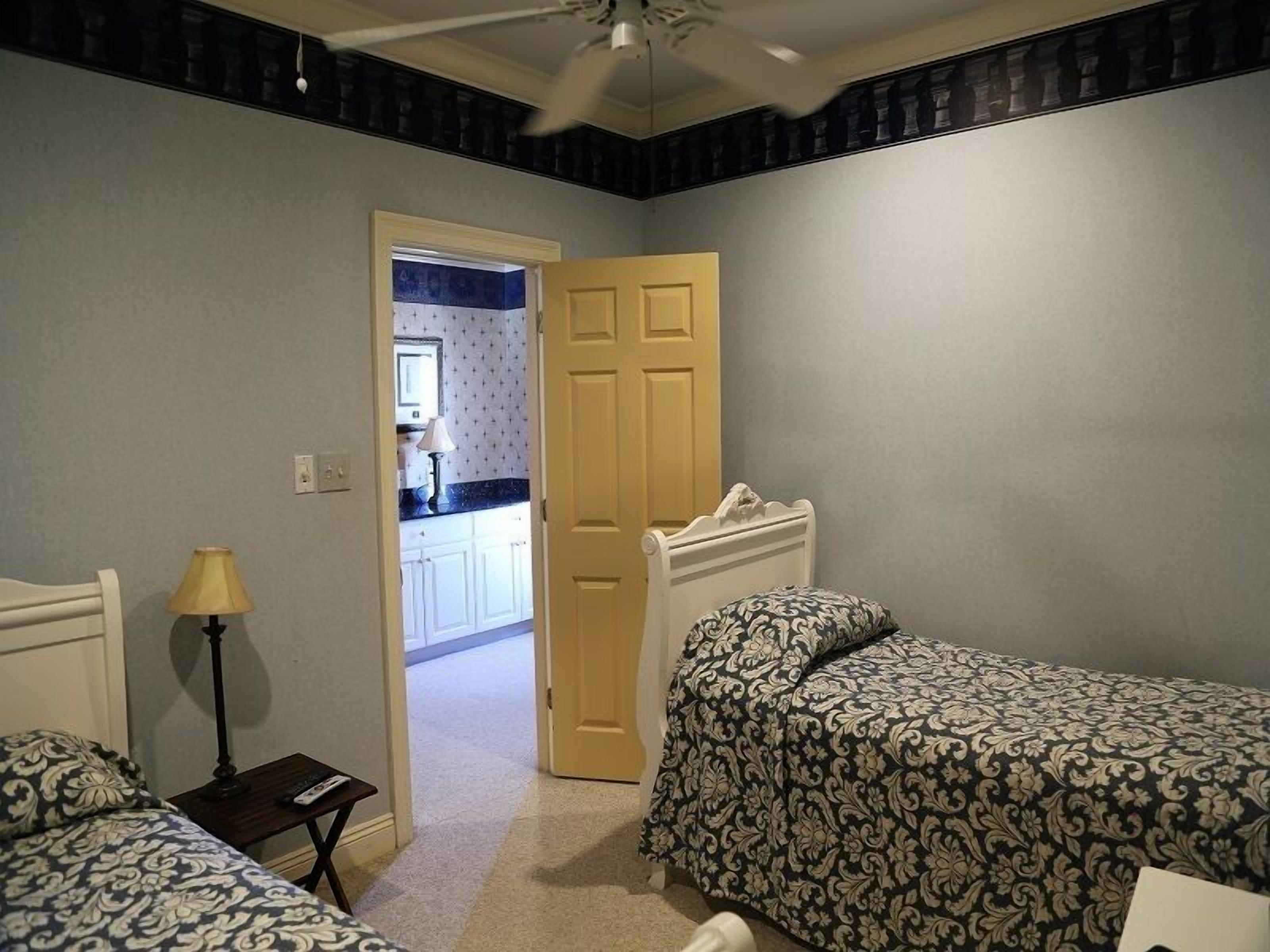 Un dormitorio con dos camas, una mesita de noche, una lámpara y una puerta que da a un baño.