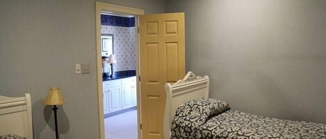 Un dormitorio con dos camas, una mesita de noche, una lámpara y una puerta que da a un baño.