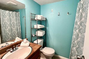 A bathroom with a teal wall, a white toilet, a sink with a mirror, and a towel rack with folded towels.