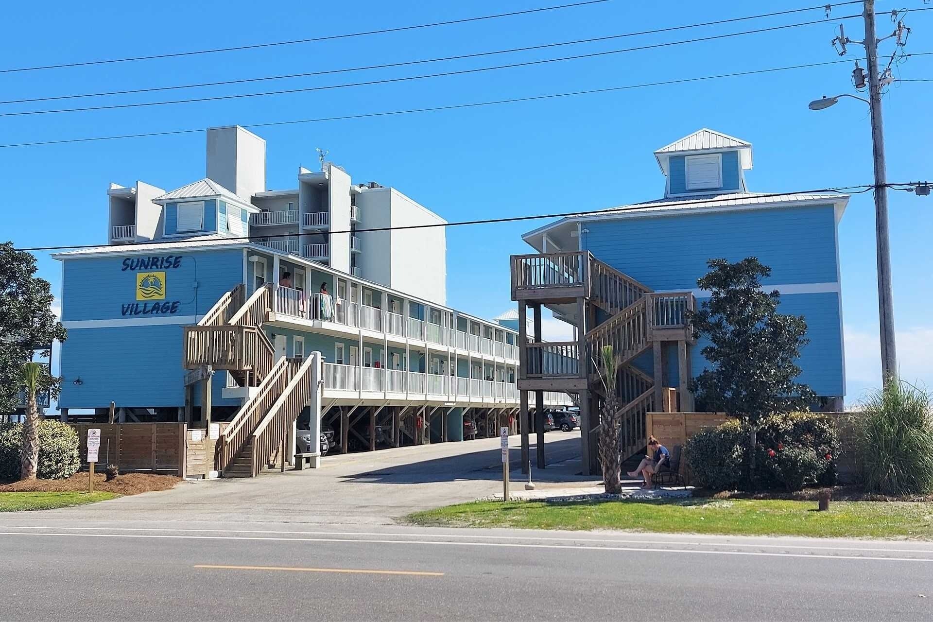 A coastal building with multiple balconies and a sign reading "Sunrise Village".