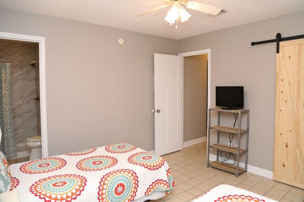 A bedroom with a bed, a television on a stand, a door, and a ceiling fan.